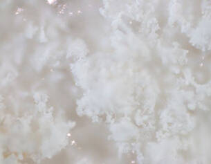 Close-up van een luchtige, witte kristallijne textuur die lijkt op sneeuw of een zachte wolk.