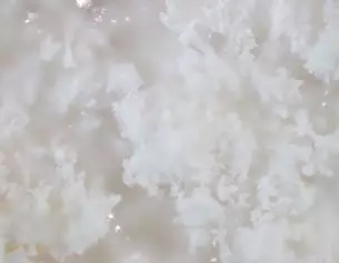 Close-up van een luchtige, witte kristallijne textuur die lijkt op sneeuw of een zachte wolk.