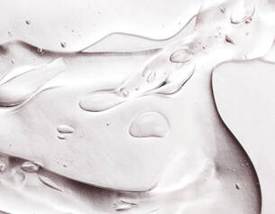 Close-up of clear gel-like substance with smooth curves and small, glistening droplets on a light background.