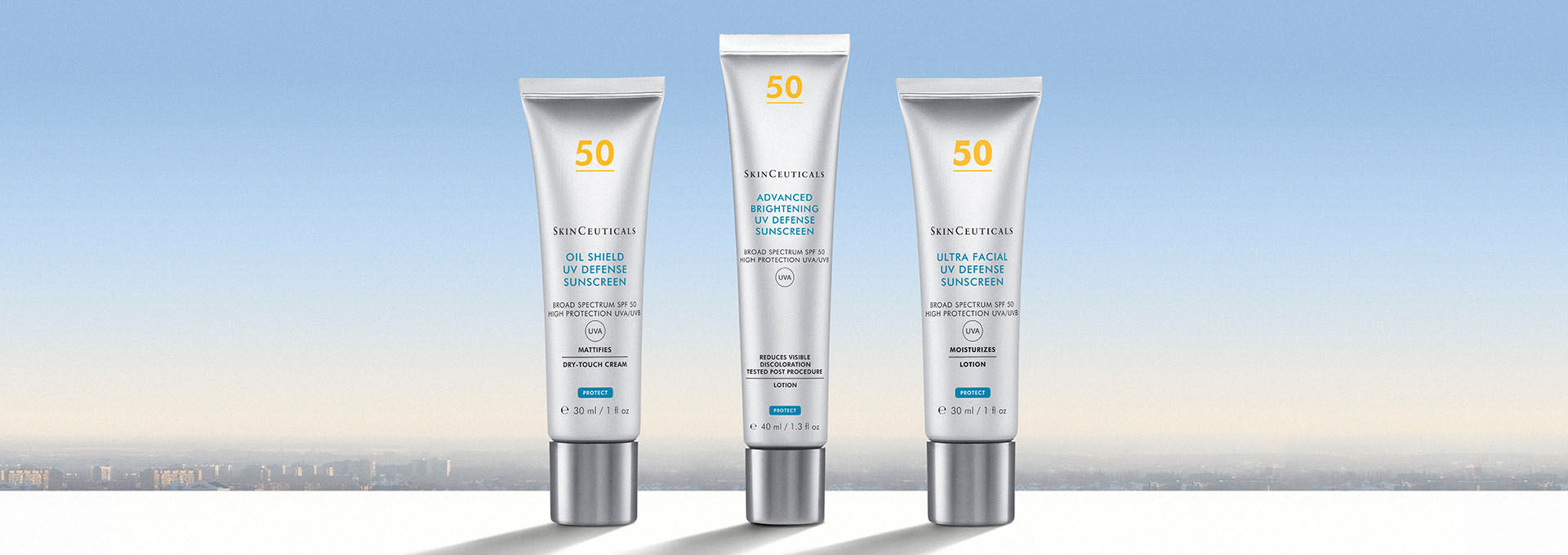 Three skincare tubes arranged on a white surface against a soft gradient background of blue and pale orange, depicting a skyline.