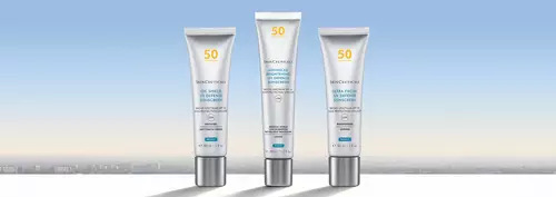 Three skincare tubes arranged on a white surface against a soft gradient background of blue and pale orange, depicting a skyline.