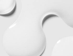 A close-up of smooth, glossy white paint droplets on a light background, showcasing their flowing and dynamic shapes.