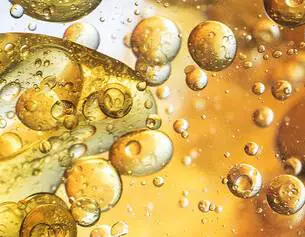 Bubbels en druppels in een gouden vloeistof, met een glanzende en abstracte achtergrond.