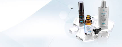 Three skincare products displayed on a clear acrylic surface, showcasing a serum, an oil, and a lotion against a light, abstract background.