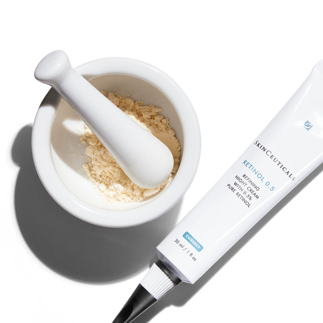 A white mortar and pestle containing a fine powder, next to a tube of SkinCeuticals Retinol 0.5 skincare cream.