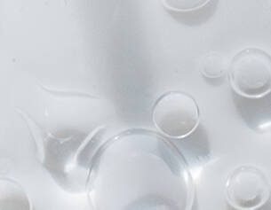 Druppels water zweven op een gladde, witte ondergrond, met verschillende formaten en helderheid.