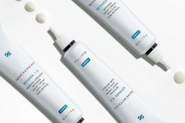 Drie tubes met Skinceuticals Retinol, met twee heldere druppels retinolcreme ernaast.