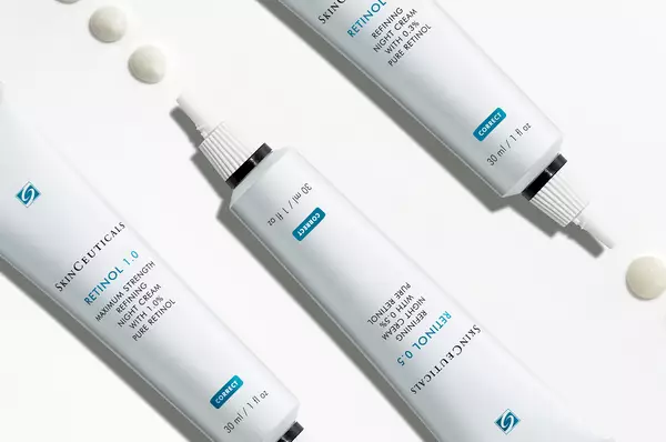 Drie tubes met Skinceuticals Retinol, met twee heldere druppels retinolcreme ernaast.