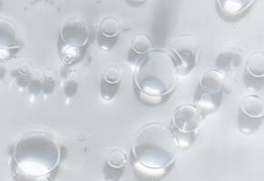 Close-up van luchtbellen in water, met heldere, reflecterende druppels op een lichte achtergrond.