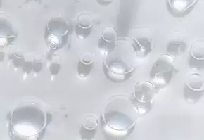 Dicht bijeenstaande luchtbellen op een helder, transparant oppervlak, met een glanzende lichtreflectie.