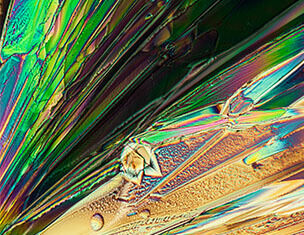 Kleurige kristallen met glinsterende patronen, gefotografeerd onder microscooplicht.