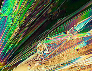 Kleurige kristallen met glinsterende patronen, gefotografeerd onder microscooplicht.