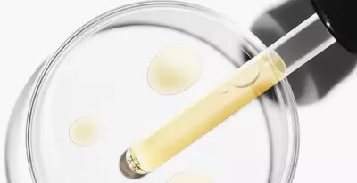Een pipet met een gele vloeistof boven een petrischaal met druppels van dezelfde vloeistof.