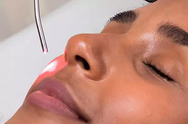 Vrouw met gesloten ogen ondergaat een huidbehandeling met een lasersysteem.