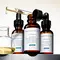 Drie flessen met huidverzorgingsserums van SkinCeuticals, waaronder C E Ferulic, Phloretin CF en Serum 10, staan op een schap met een pipet en een glazen houder.