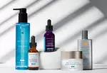 Verzorgingsproducten van Skinceuticals op een lichte achtergrond met schaduwen. Inclusief reiniger, serums en zonnebrandcreme.