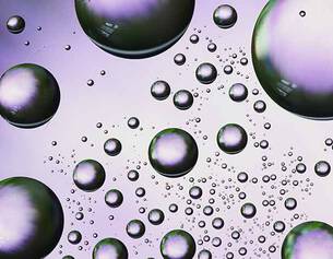 A close-up of iridescent bubbles of varying sizes against a soft purple background, creating a dynamic, airy effect.