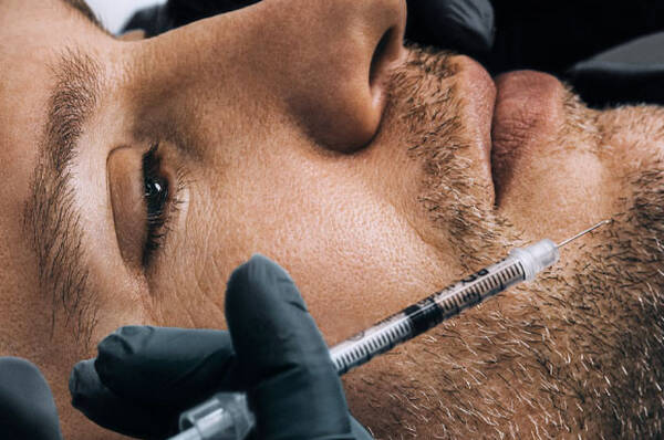 Een close-up van een man met een injectienaald dichtbij zijn gezicht, terwijl een verpleegkundige het procedure uitvoert.