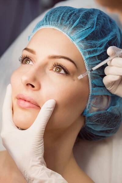 Een vrouw met een verpleegstershoedje en handschoenen ontvangt een cosmetische behandeling met een injectiespuit.