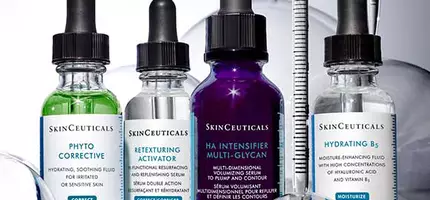 Vier flacons met huidverzorgingsserums van SkinCeuticals, waaronder Phyto Corrective, Retexturing Activator, HA Intensifier Multi-Glycan en Hydrating B's, met druppelaars en een glazen pipet op een lichte achtergrond.