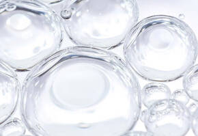 Heldere waterdruppels met luchtbellen op een lichte achtergrond, weerkaatsend en glinsterend.