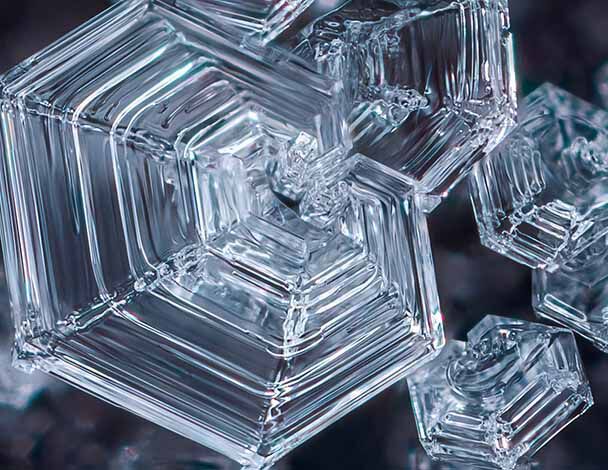 Close-up of intricate, transparent ice crystals with hexagonal shapes, showcasing their natural geometric patterns.