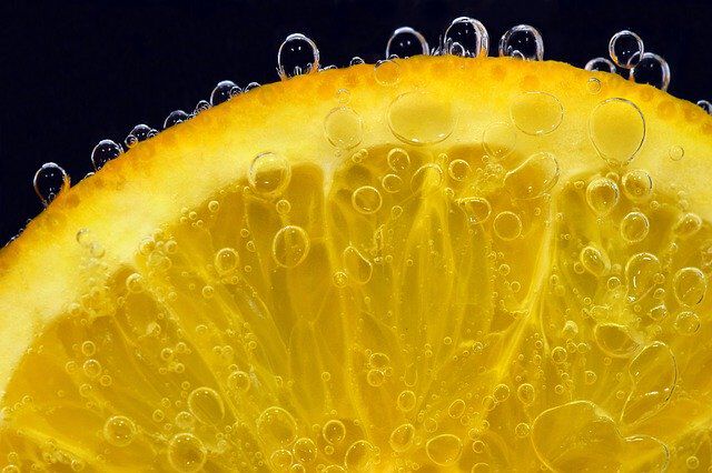 Close-up of a lemon slice with bubbles forming around its surface, showcasing vibrant yellow hues and juicy texture against a dark background.