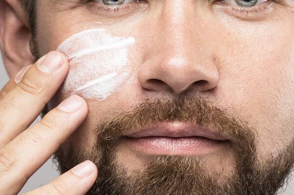 Een man met een baard brengt gezichtscreme aan op zijn gezicht.