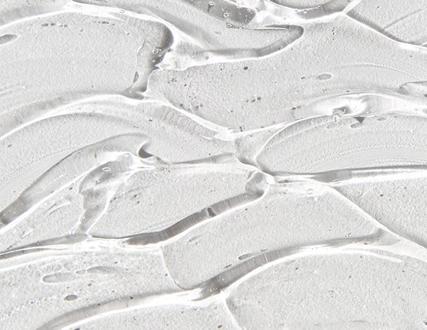 Close-up van glanzende, transparante gelachtige textuur met golvende lijnen op een witte achtergrond.