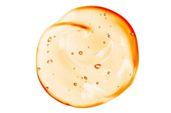 Een glanzende, doorzichtige substantie in een cirkelvormige vlek met een oranje tint en kleine luchtbelletjes.