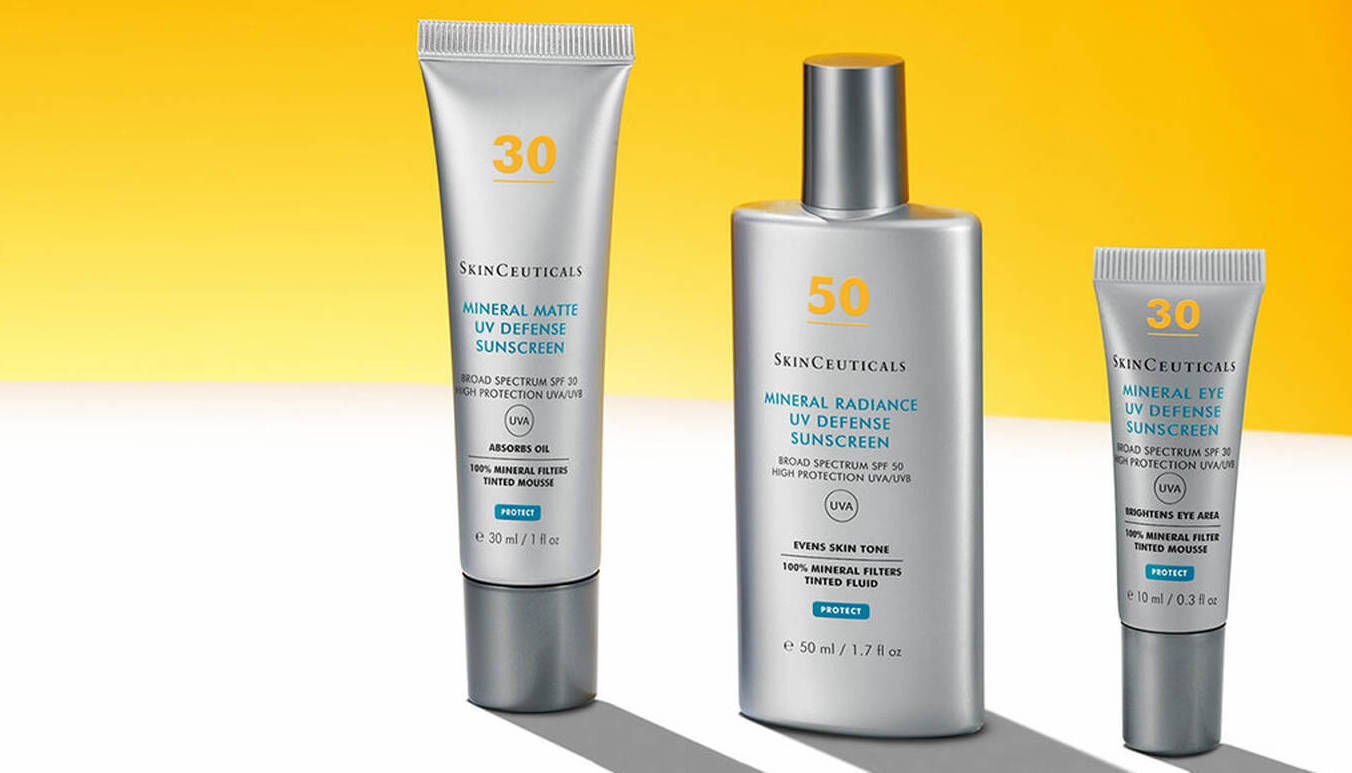 Drie tubes zonnebrandcreme van SkinCeuticals tegen een gele achtergrond: een mat, een stralend en een getint product.